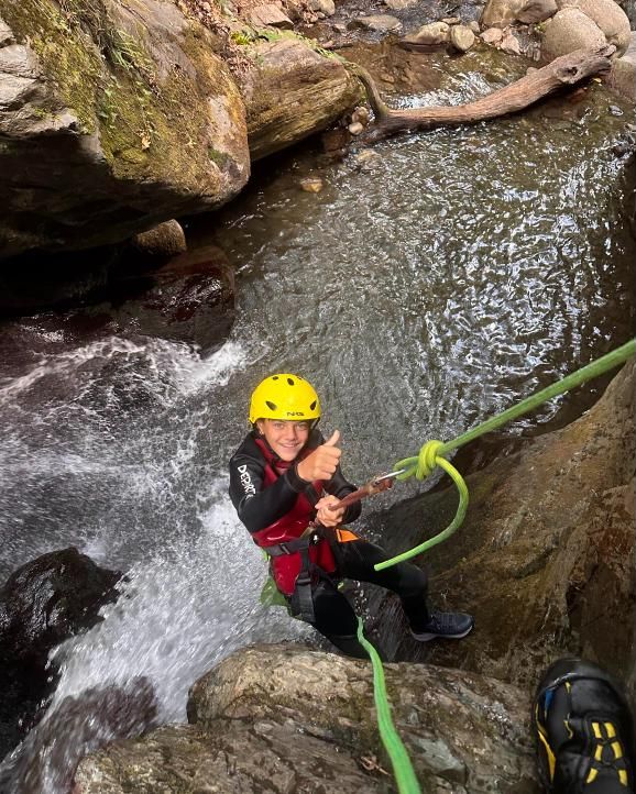 Un chico baja en rápel junto a una cascada y levanta el pulgar